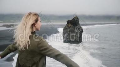 自由：年轻美丽的女人站在黑滩的岸边，靠近大海，看风景。